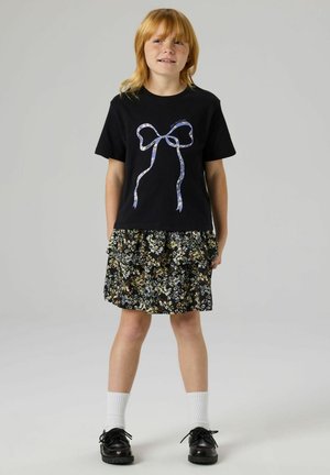 Black t-shirt with a blue and white ribbon bow graphic, paired with a black floral ruffled skirt. Accessories include white socks and black shoes.