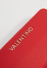 Červená kožená peňaženka s textúrovaným povrchom a zlatým embosovaným logom "VALENTINO" na prednej strane.