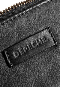 Juodas odinis piniginė su tekstūruotu paviršiumi, turinti auksinį užtrauktuką ir įspaustą etiketę su užrašu "Depeche."
