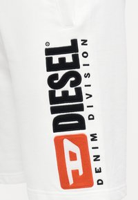 Weiße Baumwollshorts mit schwarzer und orangefarbener Stickerei. Der Schriftzug "DIESEL" ist deutlich sichtbar, ebenso wie "DENIM DIVISION".