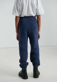 Tumši zili vilnas sporta bikses ar elastīgu jostu un aprocēm pie potītēm, kombinētas ar pelēku pārizmēra T-kreklu un melniem, masīviem zābakiem.