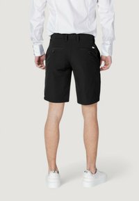Pantalones cortos negros de corte recto, fabricados en un tejido ligero, que cuentan con dos bolsillos traseros y se combinan con zapatillas blancas.