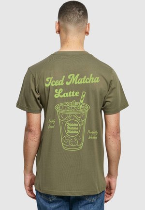 Olíva zöld póló, melynek nagy, világoszöld grafikája van egy jeges matcha latte-ról szöveggel, kerek nyakkivágással és rövid ujjakkal.