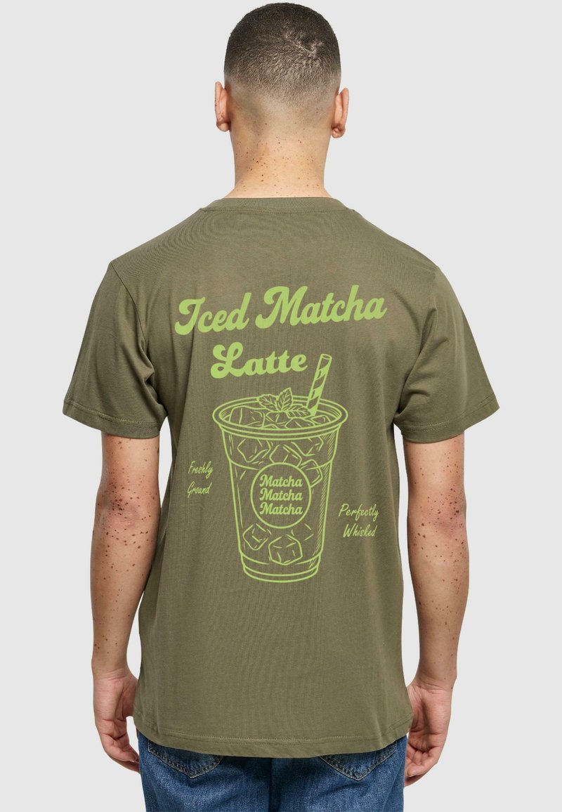 Oliven grøn t-shirt med et stort, lys grønt grafisk motiv af en iset matcha latte med tekst, rund halsudskæring og korte ærmer.