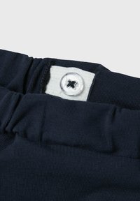 Elastische marineblauwe tailleband met verstelbare knoop op witte stoffen strip voor maatregeling van kleding.