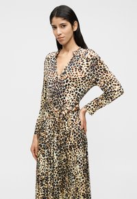 Μάξι φόρεμα με λεοπάρ μοτίβο, μακριά μανίκια και ντεκολτέ σε σχήμα V. Κατασκευασμένο από λείο ύφασμα με ζώνη στη μέση για να τονίζει τη σιλουέτα.