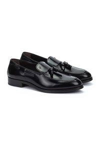 Mocasines de cuero negro presentan una textura suave, borlas decorativas, detalles de costura y un tacón bajo para facilitar su uso.