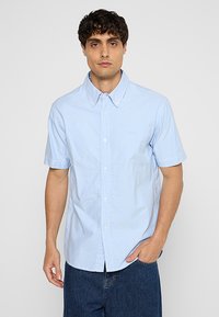 Camicetta azzurra a maniche corte con colletto button-down, realizzata in tessuto di cotone, presenta un piccolo logo sul lato sinistro del petto e una chiusura con bottoni.