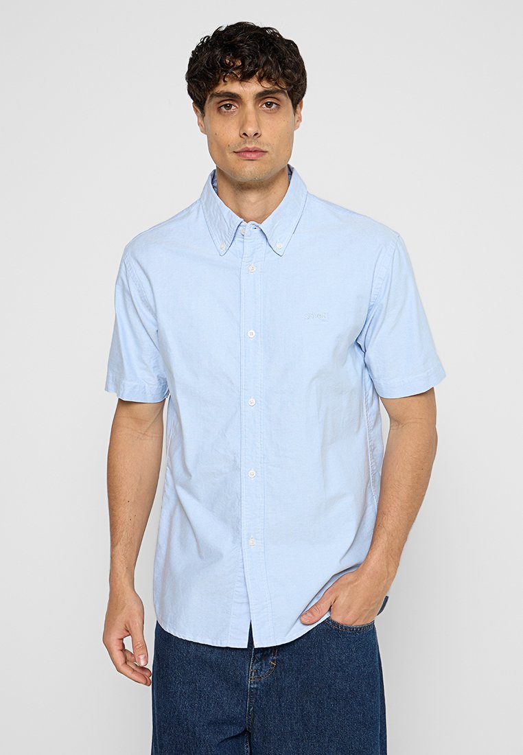 Camicetta azzurra a maniche corte con colletto button-down, realizzata in tessuto di cotone, presenta un piccolo logo sul lato sinistro del petto e una chiusura con bottoni.