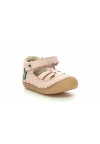 Zapato de cuero rosa claro con punta redonda, correa ajustable y diseños de cortes en los lados. Presenta una suela de goma.