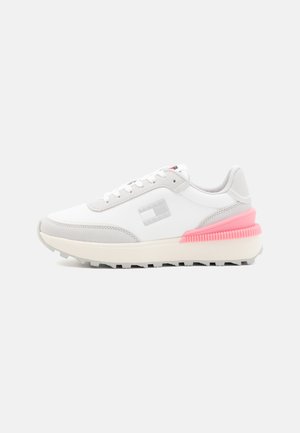 Zapatilla blanca con acentos grises, material texturizado, detalle en el talón rosa y suela con patrón. Los cordones y el logo en el costado completan el diseño.