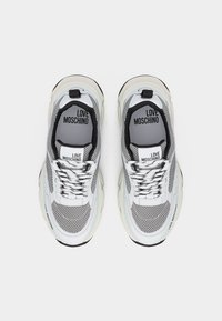 Ζευγάρι λευκά και μαύρα αθλητικά παπούτσια Love Moschino με λεπτομέρειες από διχτυωτό υλικό και εσωτερικές σόλες με το λογότυπο, φαίνονται από πάνω σε λευκό φόντο.
