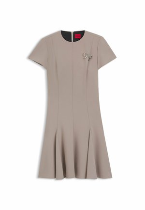 Beiges Kleid mit kurzen Ärmeln, gerader Schnitt, A-Linien-Saum und Falten. Es hat eine silberne Schleifenapplikation und einen verdeckten Reißverschluss auf der Rückseite.