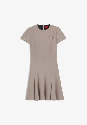 Beige dress with short sleeves, straight cut, A-line bottom, and pleats. Features a silver bow accent and a concealed zip at the back.