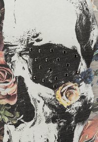 Tela gráfica con un cráneo rodeado de rosas, con tachuelas negras dispuestas en un patrón. El color base es gris claro con acentos florales.