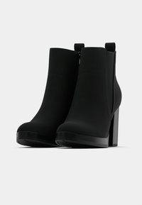 Czarne botki za kostkę z gładką powierzchnią, wysokim szerokim obcasem i zamkiem błyskawicznym. Projekt jest elegancki, z zaokrąglonym noskiem i pętelką do łatwego zakładania.
