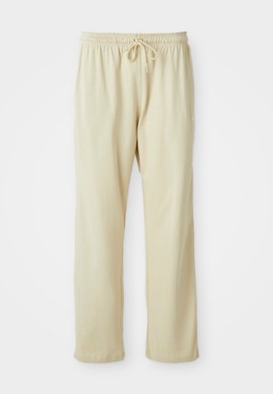 Pantaloni sportivi color beige chiaro con vita regolabile, gambe affusolate e una texture morbida. Presentano un logo del brand discreto sulla parte inferiore della gamba.