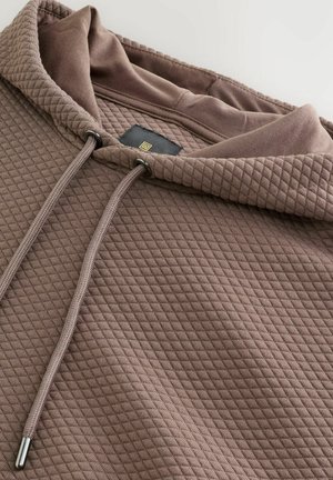 Pruun kapuutsiga pusa, mis on valmistatud tekstuurse kangaga ja millel on teemantmuster. Varustatud metallotsikutega nööriga ja sildiga sisemisel kaeluse juures.