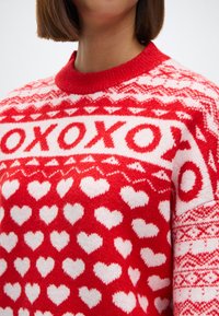 Suéter rojo de punto con patrones de corazones blancos y el texto "XOXO", con un cuello acanalado rojo y una tela texturizada.