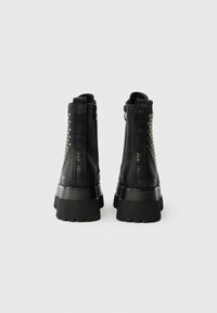 Fekete bokacipők texturált bőr felülettel, megerősített sarkal és platformtalppal. Hálós részletek az oldalakon és dombornyomott márkázás a hátulján.