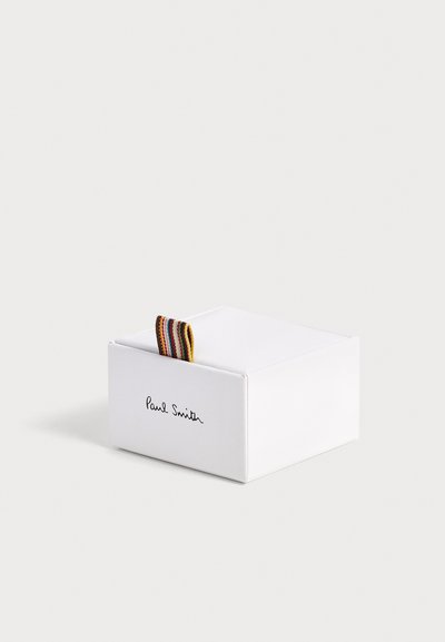 Boîte rectangulaire blanche de marque Paul Smith avec une languette en tissu rayée multicolore sur un fond clair.