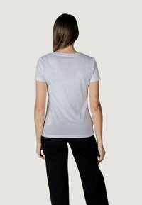 T-shirt bianco a maniche corte con colletto rotondo e un design aderente, abbinato a pantaloni neri. Tessuto dalla consistenza liscia.