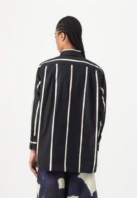 Black shirt with vertical white stripes, featuring a spread collar, buttoned cuffs, and a relaxed fit, made from a lightweight fabric.