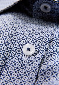 Marineblauw-wit patroonhemd met een close-up van een plastic knoopje met een stervormig gat en een gladde stoftextuur.