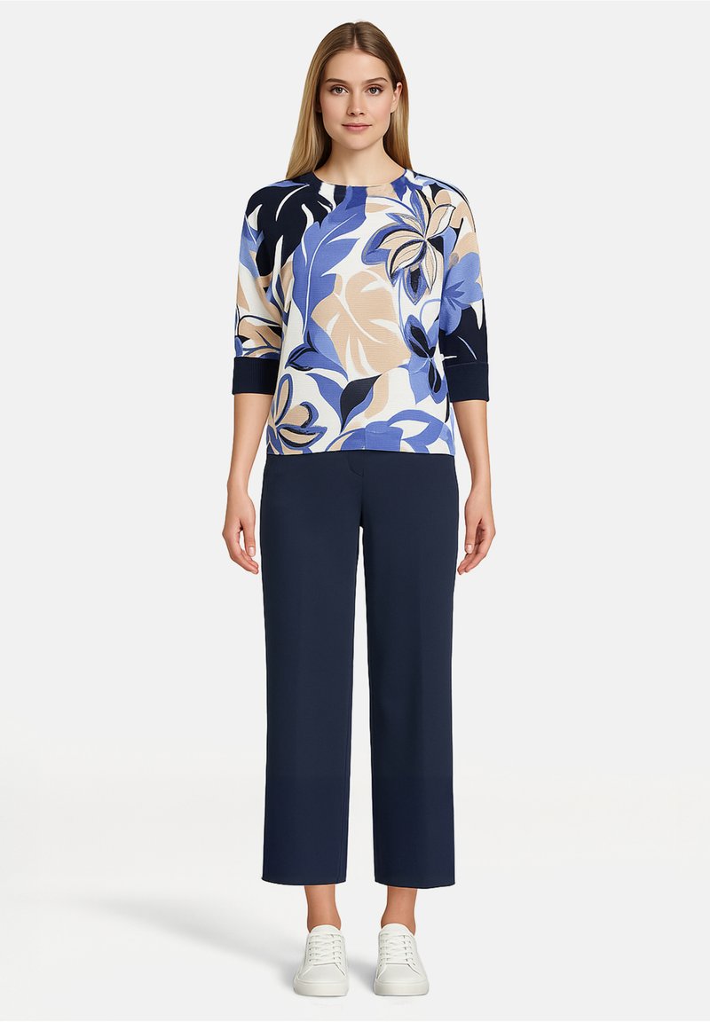 Haut en maille à fleurs bleu, beige et marine, avec des manches trois-quarts. Associé à un pantalon large marine et des baskets blanches.