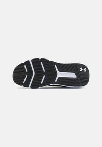 Črno atletiko čevljev podplat z teksturirano gumo, ki ima herringbone vzorec in bele poudarke. Logotip Under Armour blizu pete.