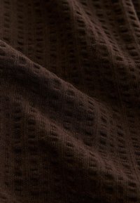Dark brown textured fabric with a soft, raised pattern creating subtle shadows and folds across the surface.