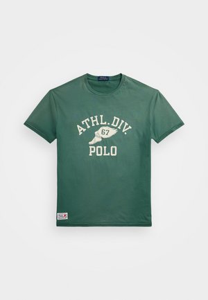 Grünes T-Shirt mit kurzen Ärmeln, weißem Schriftzug ATHL. DIV. 67 POLO und geflügeltem Schuhmotiv auf der Brust, kleines Patch nahe dem unteren Saum.