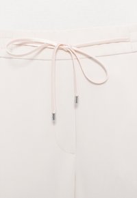 Gros plan sur un pantalon rose clair avec un cordon fin noué en nœud à la taille et des embouts métalliques argentés sur les cordons.