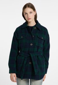 Giacca a scacchi in verde scuro e blu marino, con due tasche sul petto, chiusura con bottoni, colletto ampio e una cintura coordinata in vita.