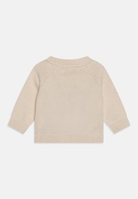 Beżowy sweter na drutach z długimi rękawami, prążkowanymi mankietami i dołem. Posiada okrągły dekolt i subtelną fakturę na całej tkaninie.