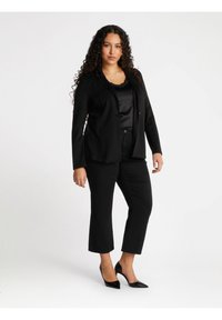 Blazer nero su misura con dettagli scintillanti, indossato sopra un top in satin nero e abbinato a pantaloni cropped neri e décolleté nere a punta.