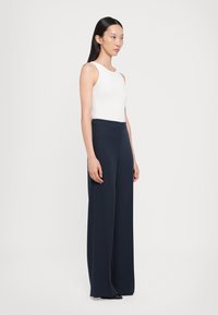 White sleeveless top and navy wide-leg trousers, made from smooth fabric. Trousers feature a high waist and flowy silhouette.