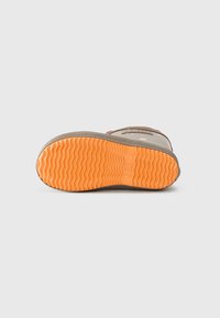 Suela de goma con un patrón ondulado; color naranja en la parte inferior; borde texturizado; unida a una parte superior impermeable en marrón y gris.