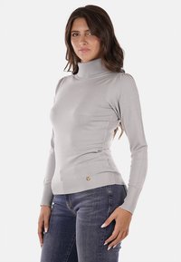 Maglione a collo alto grigio chiaro con polsini e orlo a coste, caratterizzato da un design attillato e dettagli sottili sulle spalle, indossato con jeans in denim.