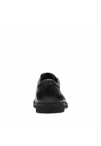 Zapato de cuero negro con una textura suave, diseño de perfil bajo, puntera redonda y un tacón minimalista. Presenta costuras sutiles y una suela de goma.