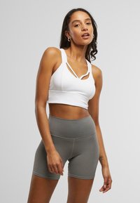 Hvit sports-BH med kryssede stropper og cropped design, kombinert med høy midje grå shorts laget av elastisk stoff.