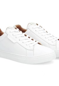 White leather sneakers with round toe, flat laces, textured sole, and minimalist design. Inner lining features a tan color for contrast.