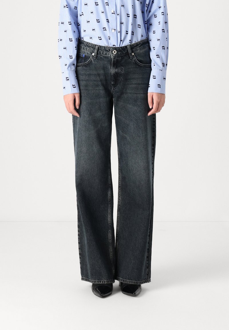 Wide-leg black denim jeans with a high waist, featuring coarse texture and slight fading. Paired with a blue button-up shirt.