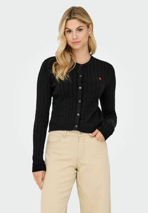 Mustavilla neulecardigan pitkillä hihoilla, pyöreällä pääntiellä ja nappikiinnityksellä. Vasemmassa rinnassa pieni punainen sydämen yksityiskohta.