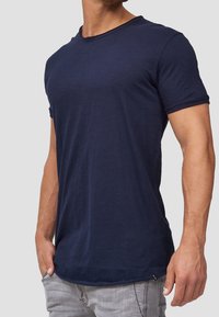 T-shirt blu navy realizzato in morbido tessuto, con scollo rotondo, maniche corte e orlo leggermente curvato. Branding minimale di lato.
