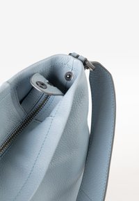 Hellblaues Ledershopping mit strukturierter Oberfläche, Reißverschluss und kurzem Tragegurt. Das Innere ist sichtbar mit glatter Fütterung und Hardware-Details.