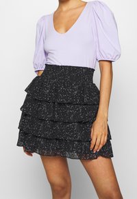 Top de manga abullonada en lavanda con escote en V profundo, acompañado de una falda negra con volantes en capas que presenta un patrón moteado en blanco.