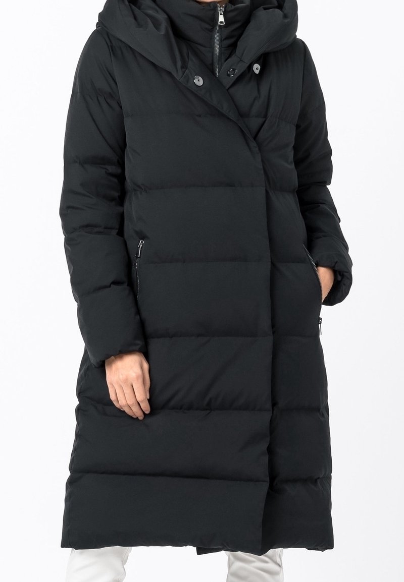 Svart vadderad jacka med huva, med en sned dragkedjestängning, sidofickor och ett quiltat mönster. Lång, lös passform för värme.