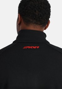 Pullover nero con un design a maglia testurizzato. Presenta un colletto alto e il logo rosso "SPYDER" sul retro.