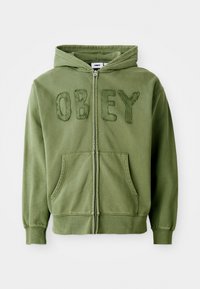 Olive green zip-up hoodie made of soft fabric, featuring the word "OBEY" in textured embroidery on the front, with side pockets and a hood.